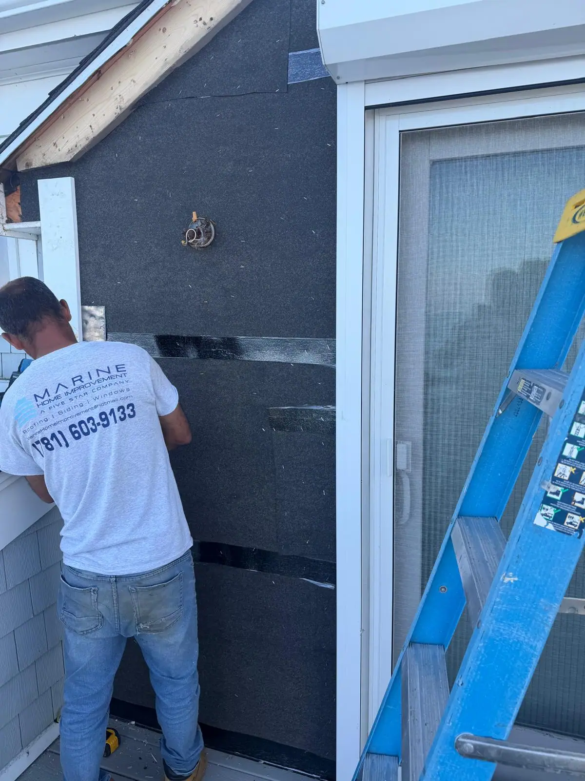 Contractor working beside exposed wall covering after siding removal near a balcony door