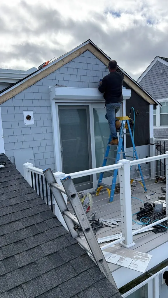 Worker installing gray shingle-style siding around a balcony door in Marshfield MA