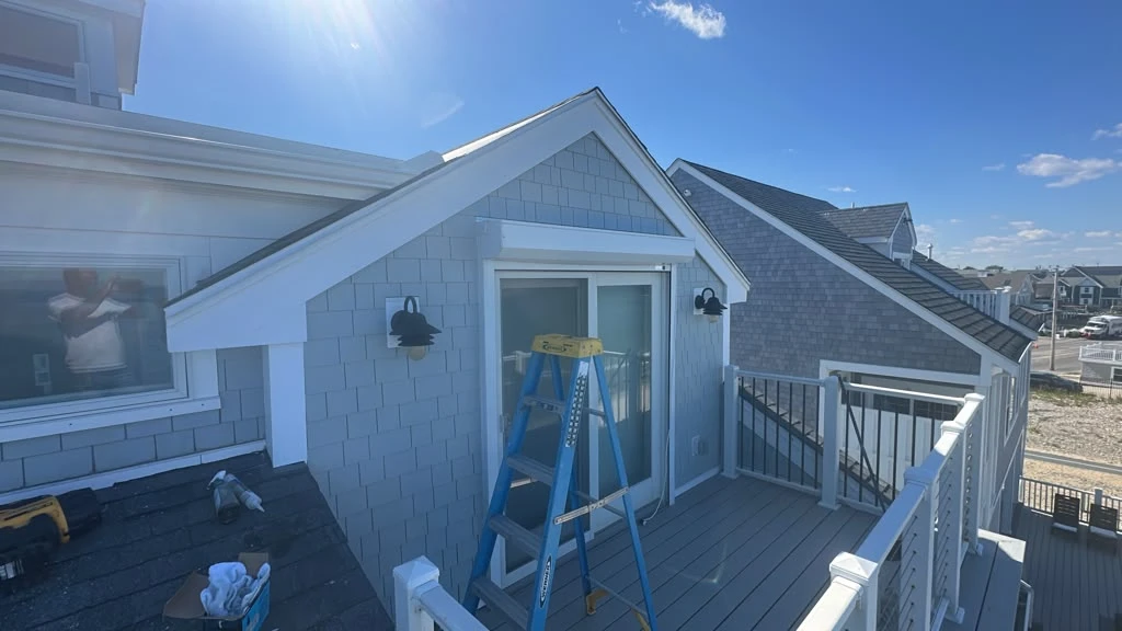 Gray shingle-style siding and white gable trim around the upper balcony door