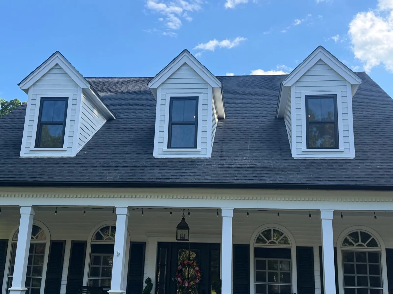Front view of three white dormers with new black windows and white trim above a covered porch.